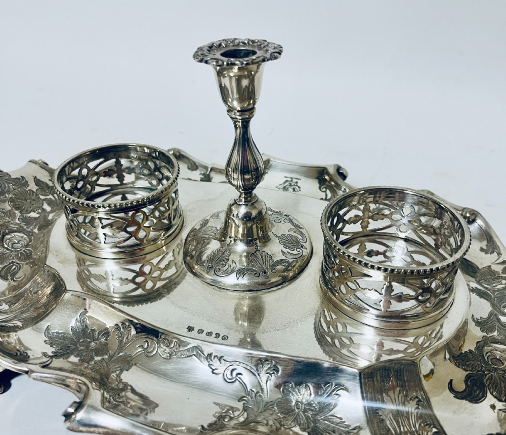 A Victorian silver-plated inkstand featuring an ornate tray with scrolled feet, two cut-glass inkwells in pierced holders, and a central taperstick. View XIX