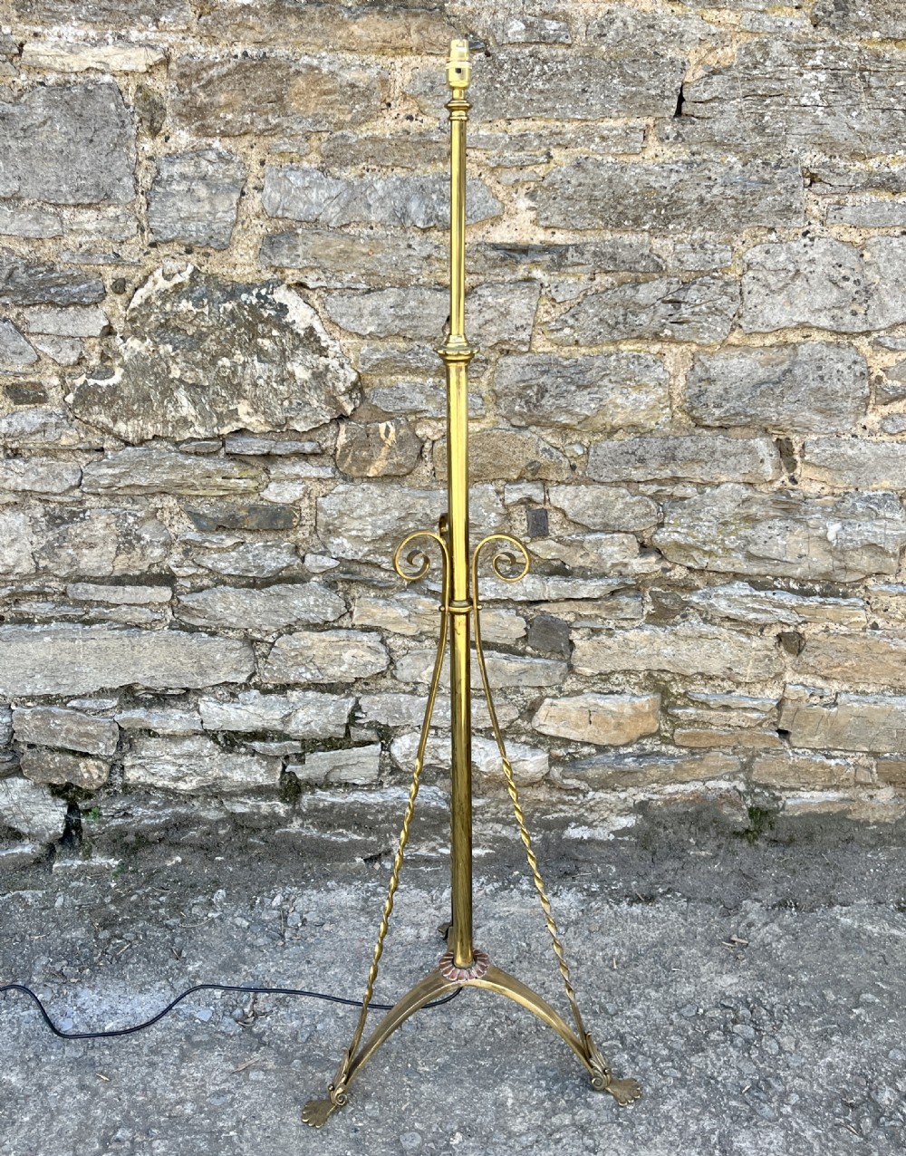 An antique brass telescopic standard lamp featuring tripod legs with scroll details and an adjustable vertical stem.