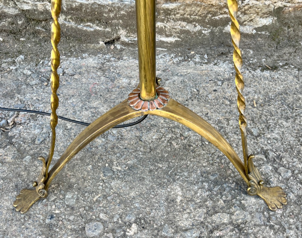 An antique brass telescopic standard lamp featuring tripod legs with scroll details and an adjustable vertical stem. View II