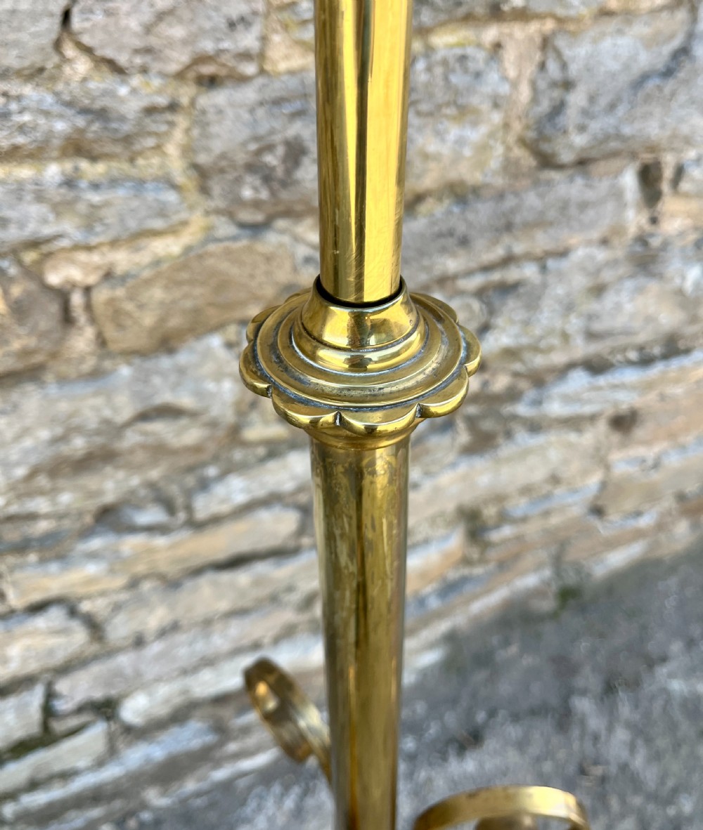 An antique brass telescopic standard lamp featuring tripod legs with scroll details and an adjustable vertical stem. View VI