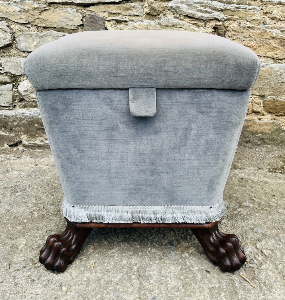 An upholstered grey velvet box ottoman featuring lower fringe trimming and dark mahogany carved lions paw feet. View II
