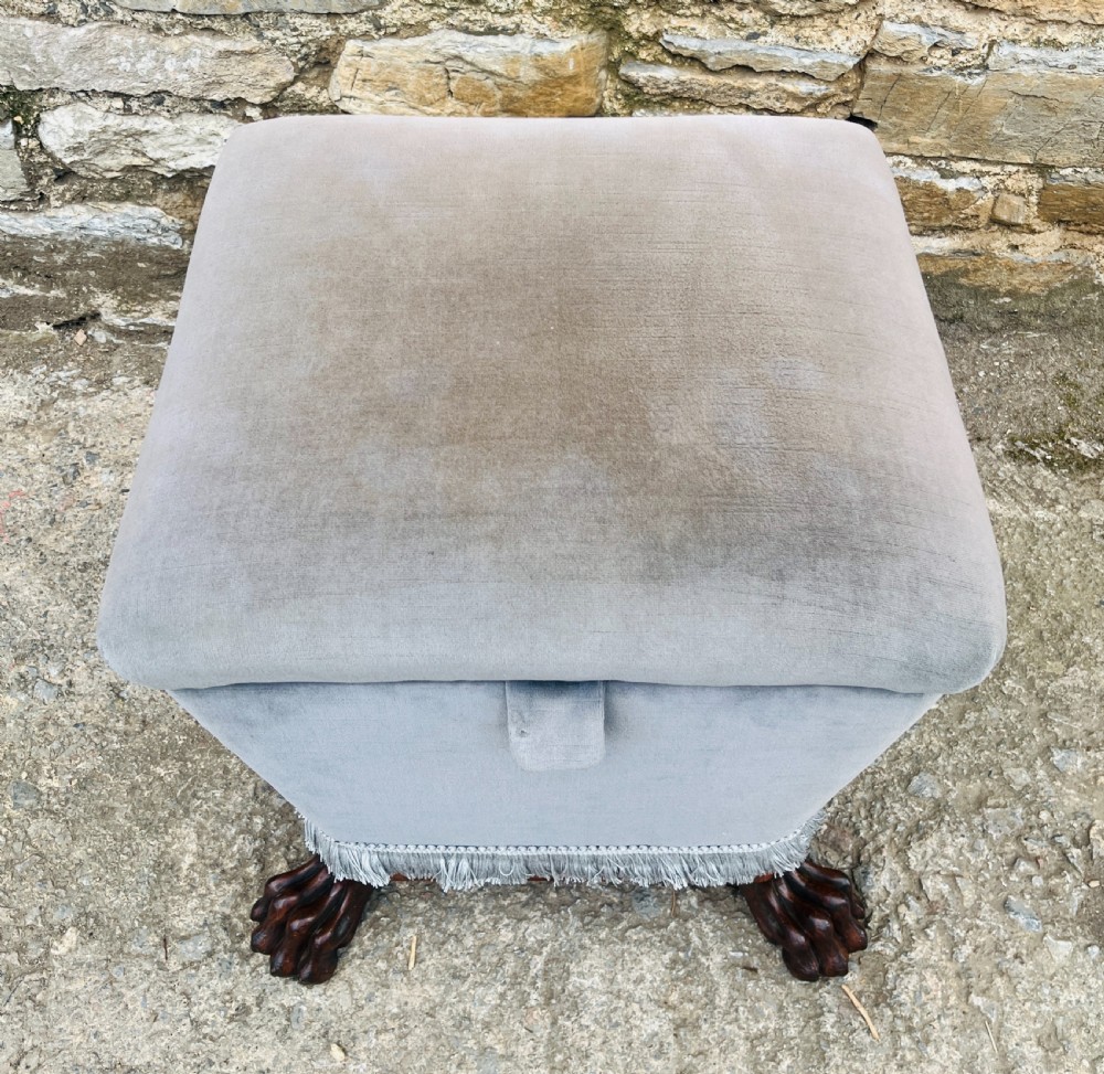 An upholstered grey velvet box ottoman featuring lower fringe trimming and dark mahogany carved lions paw feet. View III