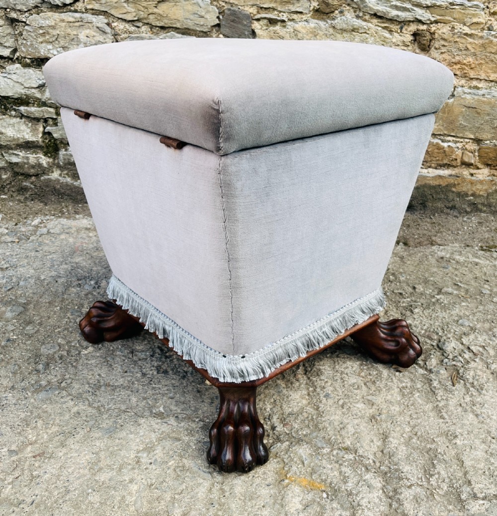 An upholstered grey velvet box ottoman featuring lower fringe trimming and dark mahogany carved lions paw feet. View X