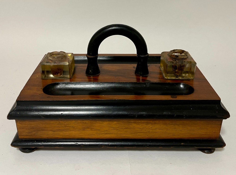 A Victorian wooden desk stand featuring two square glass inkwells, a central black arched handle, an integrated pen tray, and a single lower drawer. View V