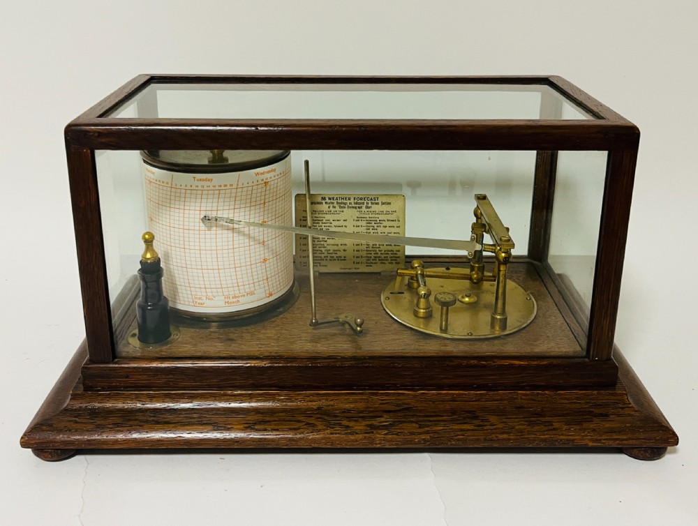 An antique barograph featuring an oak frame with glass side panels enclosing a revolving paper chart drum and polished brass mechanism.