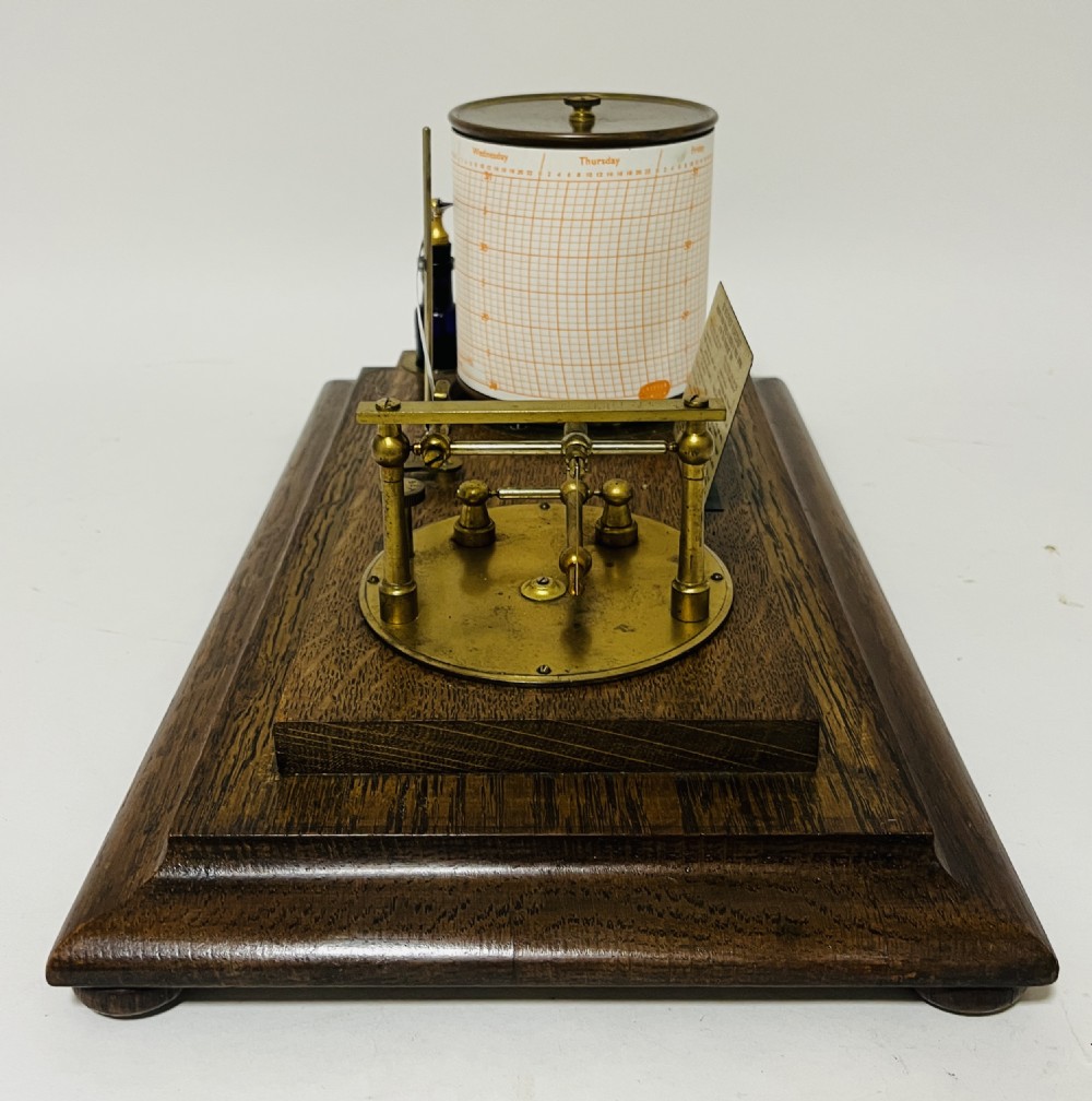 An antique barograph featuring an oak frame with glass side panels enclosing a revolving paper chart drum and polished brass mechanism. View X