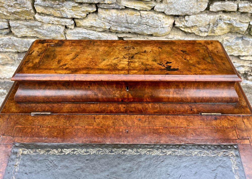 A Victorian burr walnut Davenport desk featuring a sloped writing top with a green leather insert and carved acanthus leaf front supports. View XIX