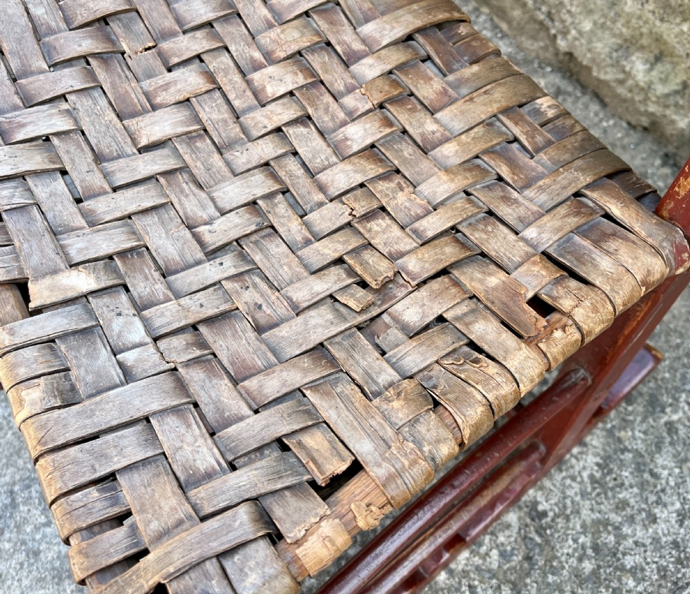 A primitive red-painted wooden rocking chair featuring a woven splint seat and scalloped back slats. View XIV