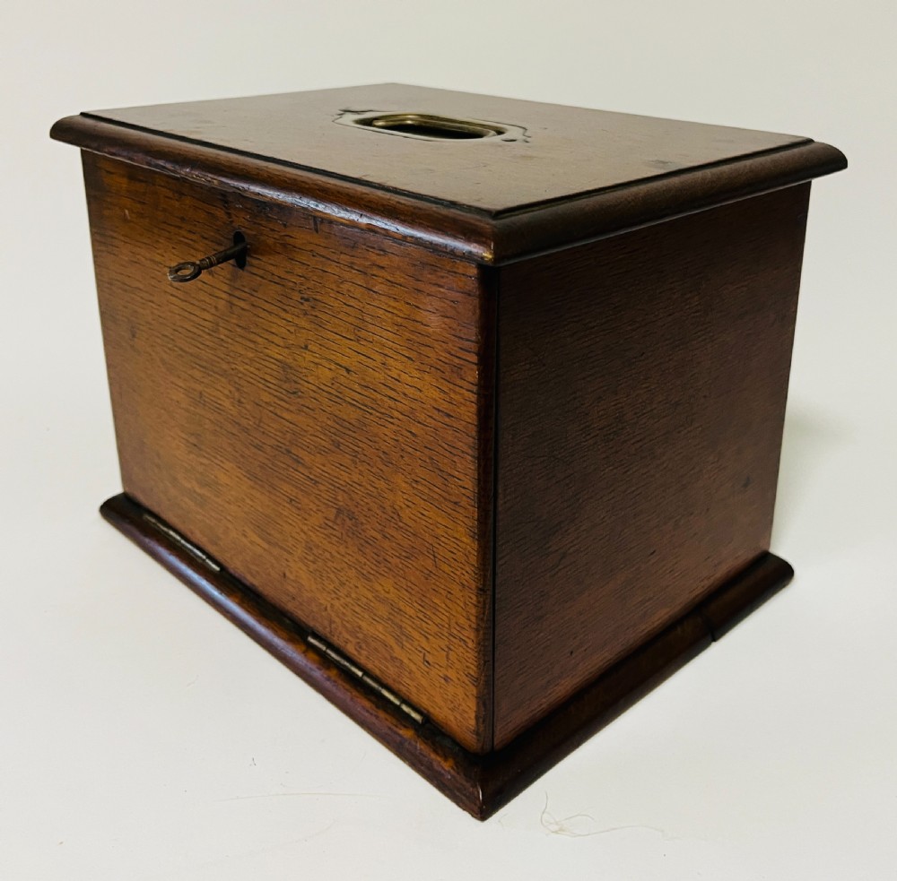 An antique oak stationery cabinet featuring a flush brass top handle, a brass keyhole with a key, and a hinged front panel. View VI