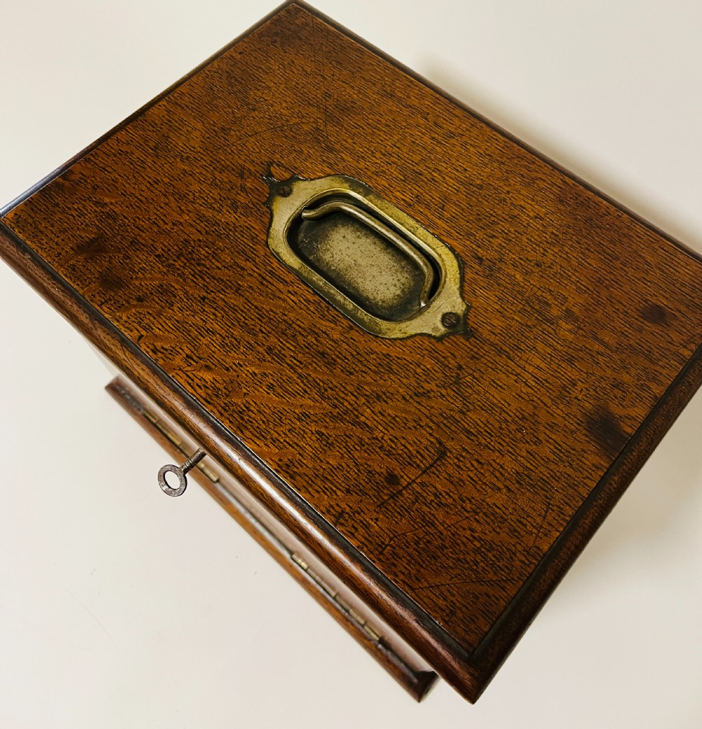 An antique oak stationery cabinet featuring a flush brass top handle, a brass keyhole with a key, and a hinged front panel. View IX