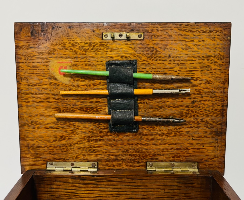 An antique oak stationery cabinet featuring a flush brass top handle, a brass keyhole with a key, and a hinged front panel. View X