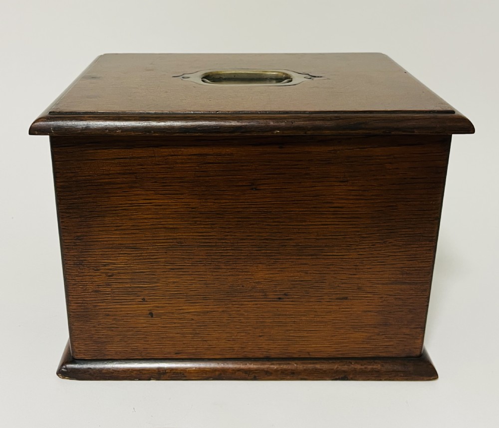 An antique oak stationery cabinet featuring a flush brass top handle, a brass keyhole with a key, and a hinged front panel. View XIII