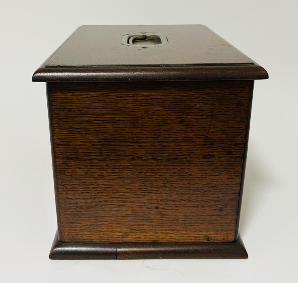 An antique oak stationery cabinet featuring a flush brass top handle, a brass keyhole with a key, and a hinged front panel. View XIV