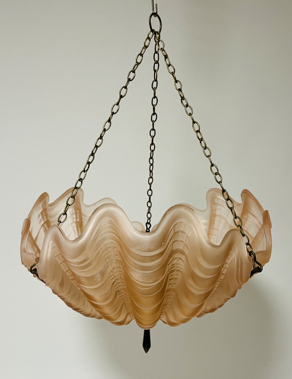An Art Deco pink frosted glass clam shell ceiling pendant light suspended by three brass hanging chains.