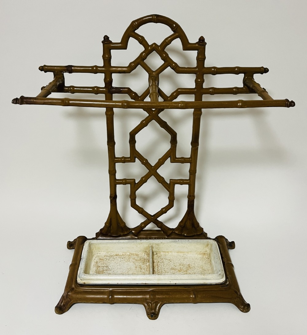 A Victorian cast iron faux bamboo umbrella stand in brown paint featuring geometric lattice backwork and a removable two-compartment drip tray.