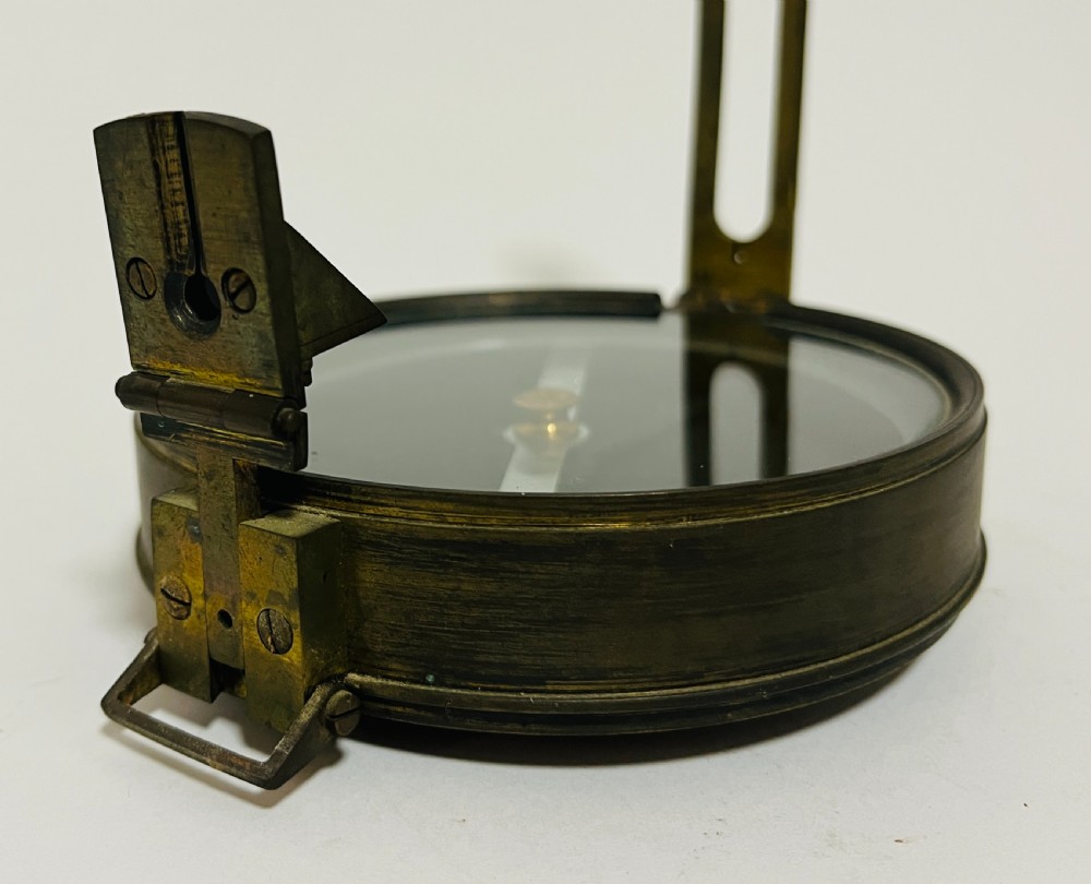 An antique brass surveying compass featuring folding sight vanes, a central needle, and a glass-covered dial. View IV