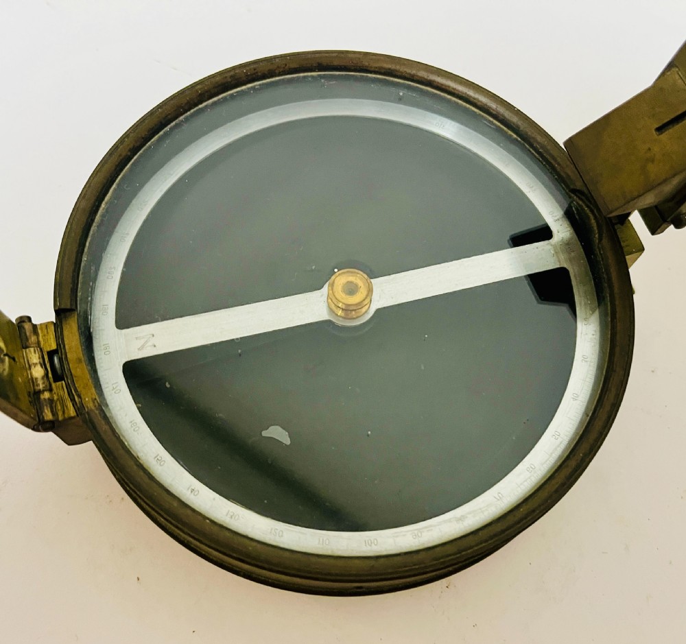 An antique brass surveying compass featuring folding sight vanes, a central needle, and a glass-covered dial. View V