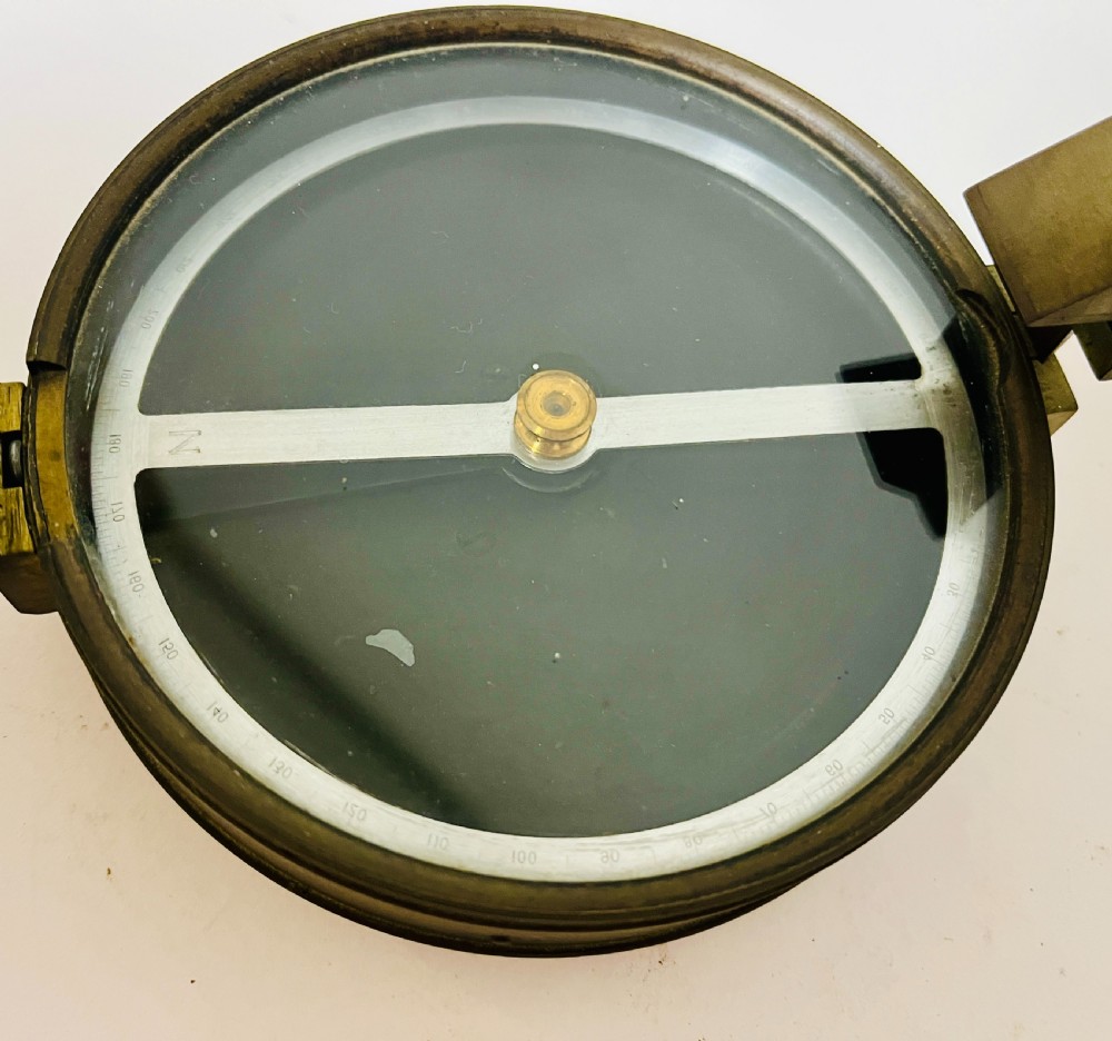 An antique brass surveying compass featuring folding sight vanes, a central needle, and a glass-covered dial. View VI
