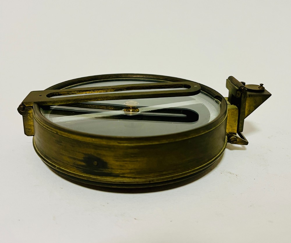 An antique brass surveying compass featuring folding sight vanes, a central needle, and a glass-covered dial. View VIII