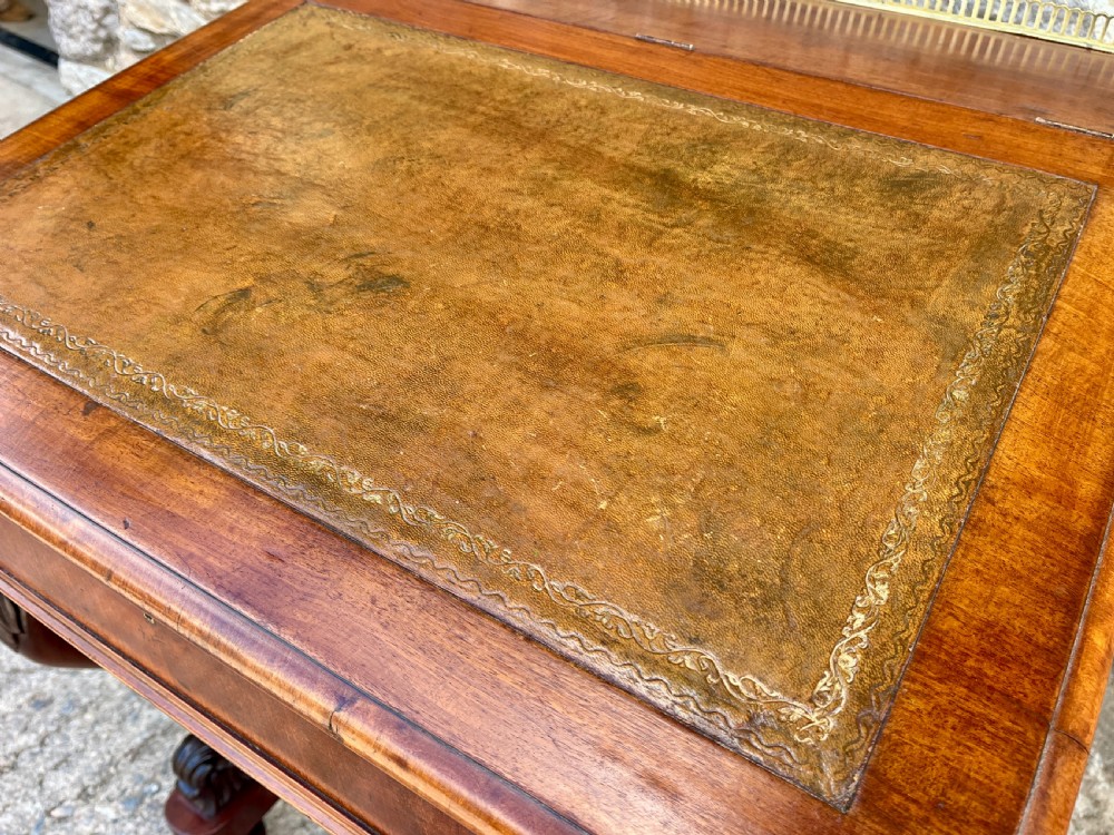 A Victorian mahogany Davenport desk featuring a sloped leather writing surface, side drawers with turned wooden knobs, a top brass gallery rail, and carved scroll front supports. View V
