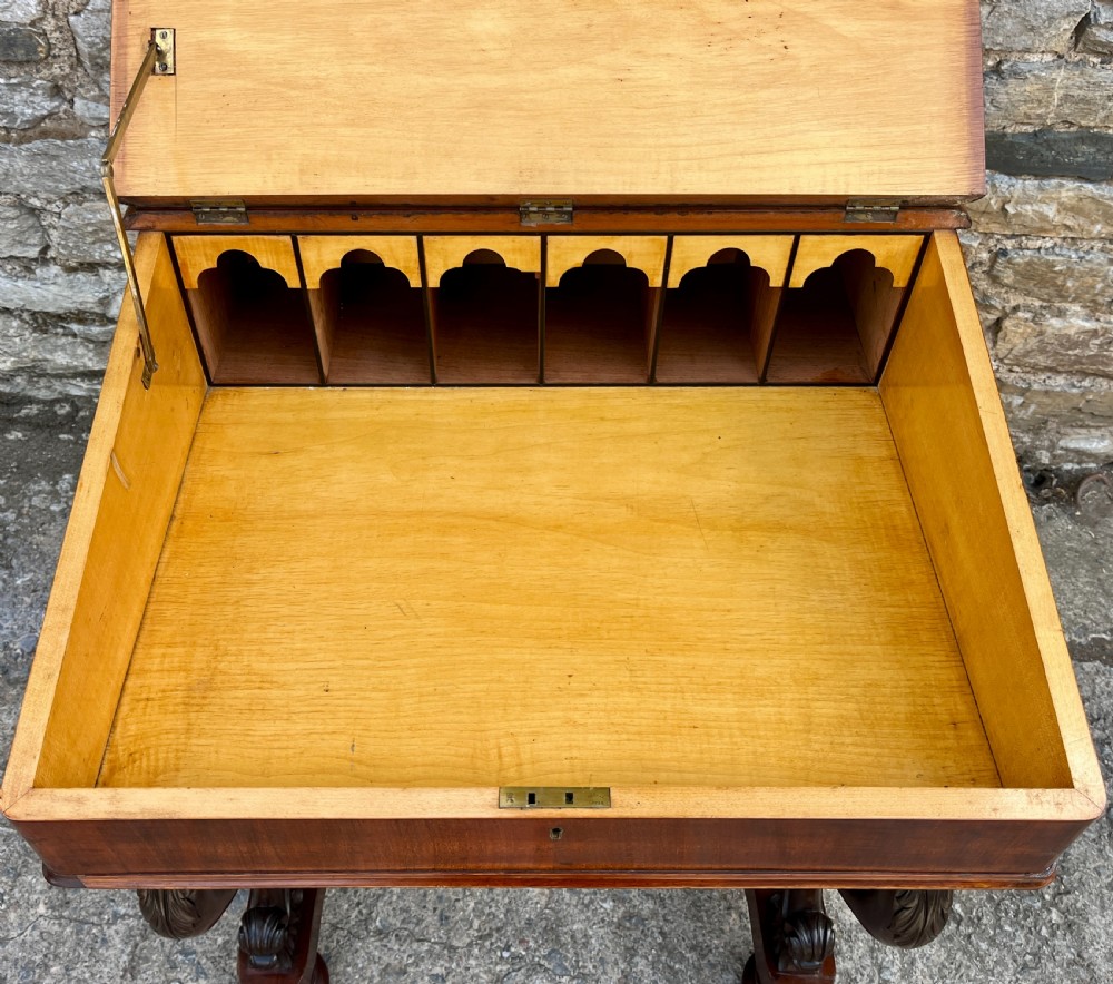 A Victorian mahogany Davenport desk featuring a sloped leather writing surface, side drawers with turned wooden knobs, a top brass gallery rail, and carved scroll front supports. View VIII