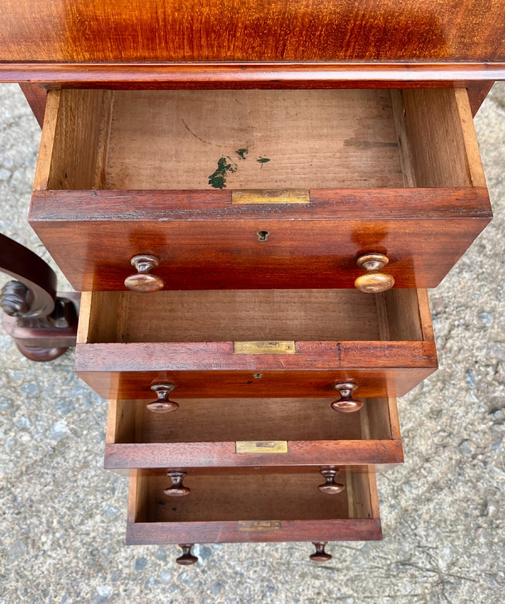 A Victorian mahogany Davenport desk featuring a sloped leather writing surface, side drawers with turned wooden knobs, a top brass gallery rail, and carved scroll front supports. View XI
