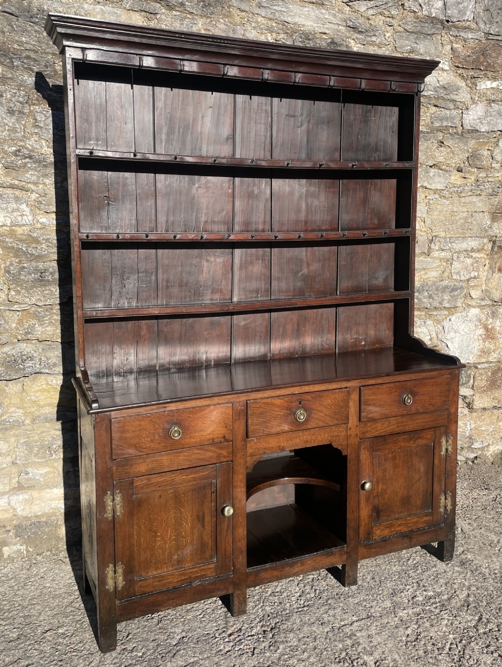 An antique dark oak Georgian dog kennel dresser featuring an open shelf rack above three drawers and two cupboard doors.
