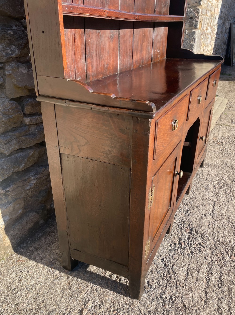 An antique dark oak Georgian dog kennel dresser featuring an open shelf rack above three drawers and two cupboard doors. View V
