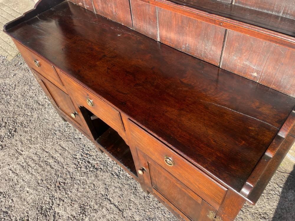 An antique dark oak Georgian dog kennel dresser featuring an open shelf rack above three drawers and two cupboard doors. View IX