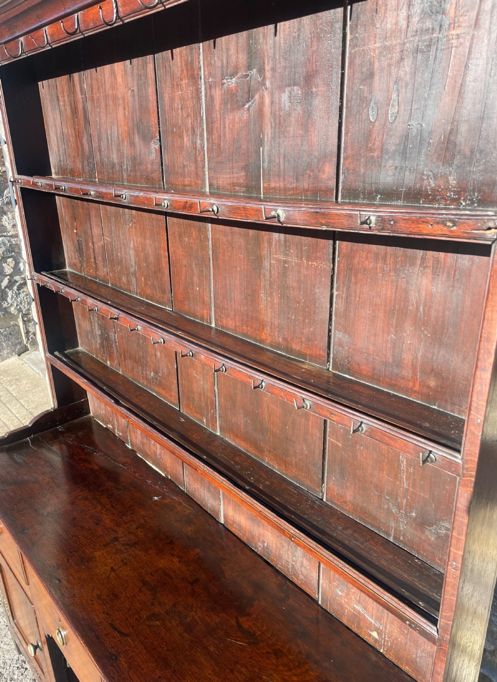 An antique dark oak Georgian dog kennel dresser featuring an open shelf rack above three drawers and two cupboard doors. View X