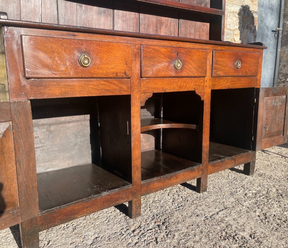 An antique dark oak Georgian dog kennel dresser featuring an open shelf rack above three drawers and two cupboard doors. View XVI
