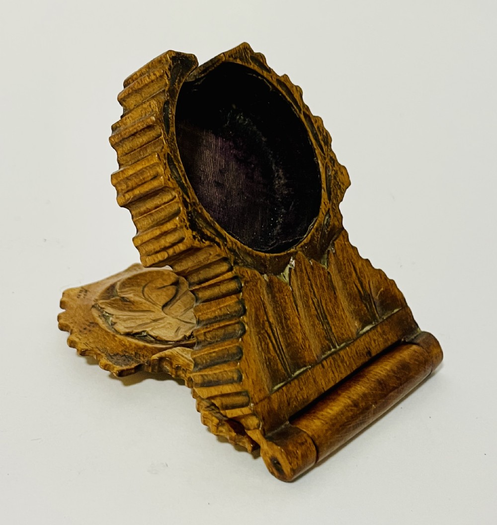 An antique carved wooden Black Forest pocket watch holder with leaf detailing on the base and a dark velvet-lined aperture for displaying a timepiece.