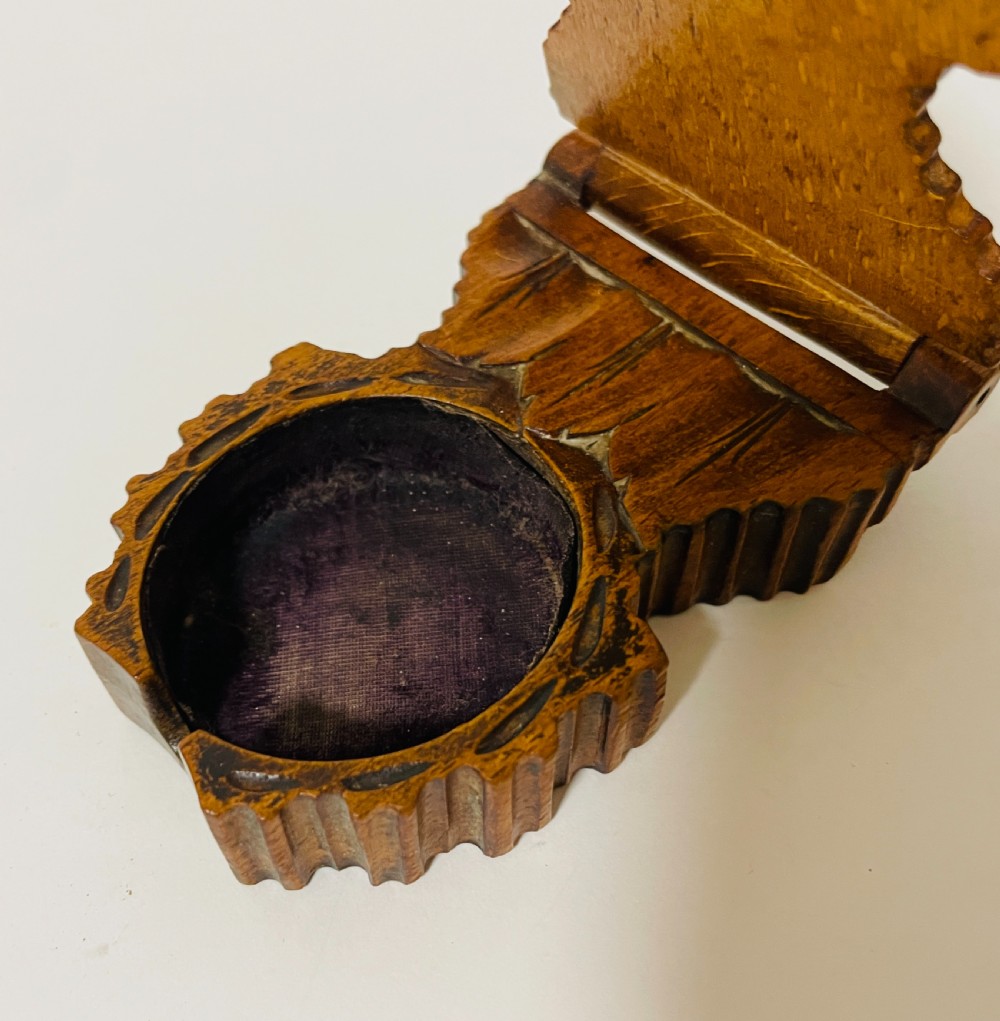 An antique carved wooden Black Forest pocket watch holder with leaf detailing on the base and a dark velvet-lined aperture for displaying a timepiece. View VI