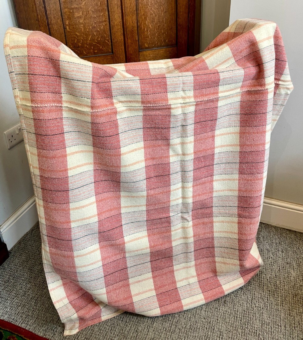 A large woven Welsh wool blanket featuring a pink, cream, and subtle yellow plaid grid design.