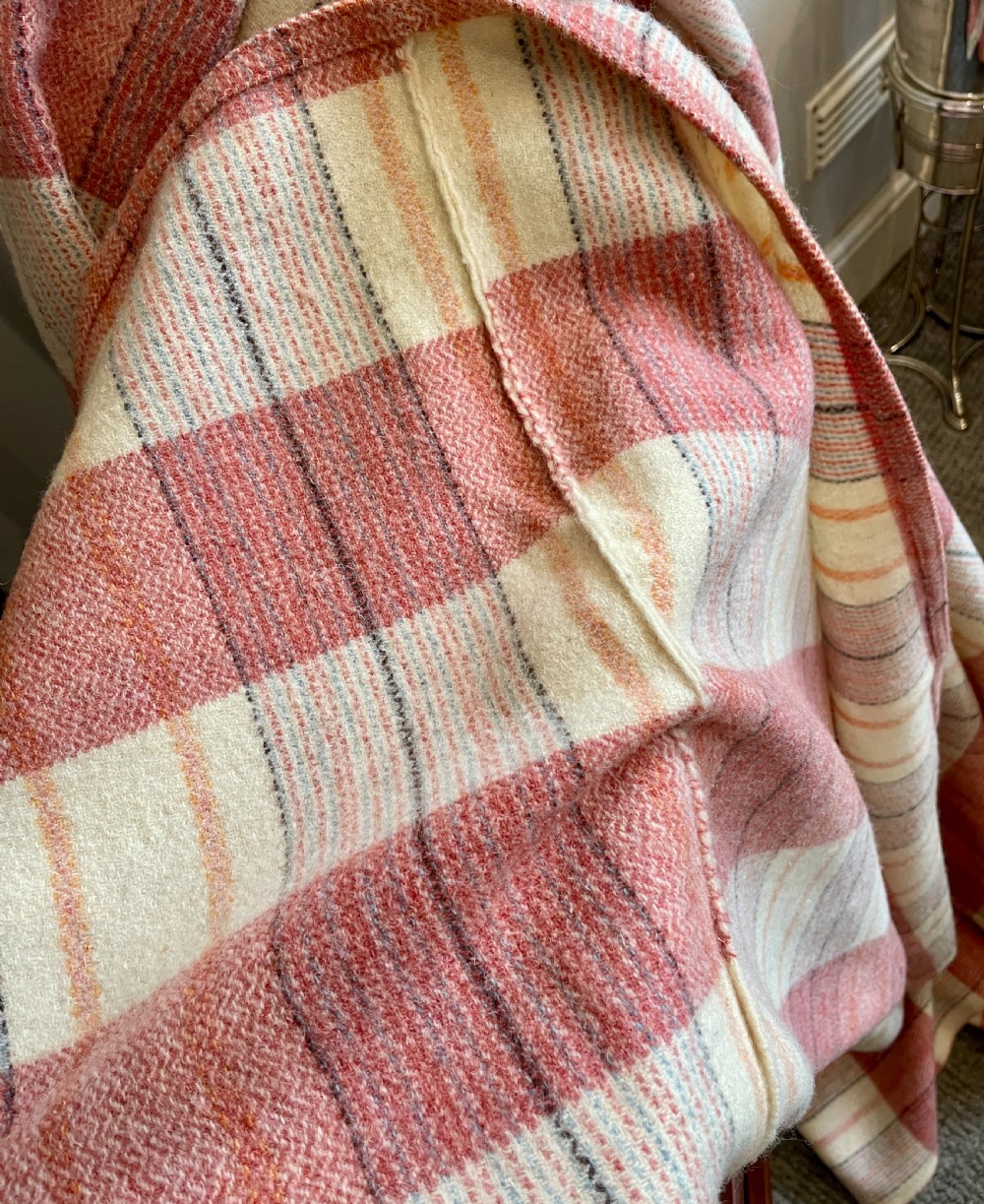 A large woven Welsh wool blanket featuring a pink, cream, and subtle yellow plaid grid design. View V