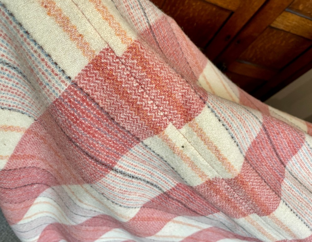 A large woven Welsh wool blanket featuring a pink, cream, and subtle yellow plaid grid design. View VI