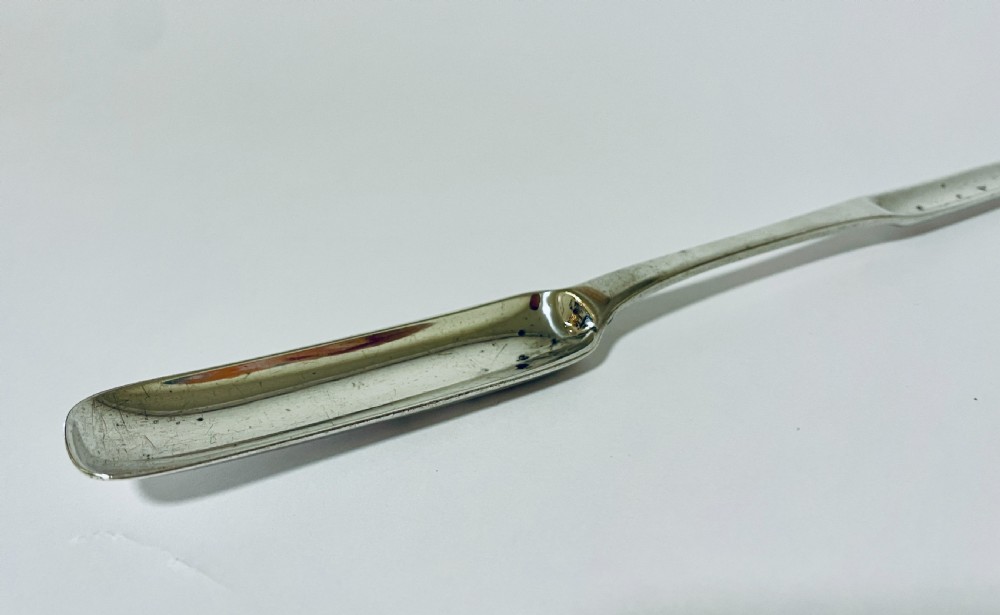 A Georgian Irish sterling silver double-ended marrow scoop resting horizontally against a plain white background. View V