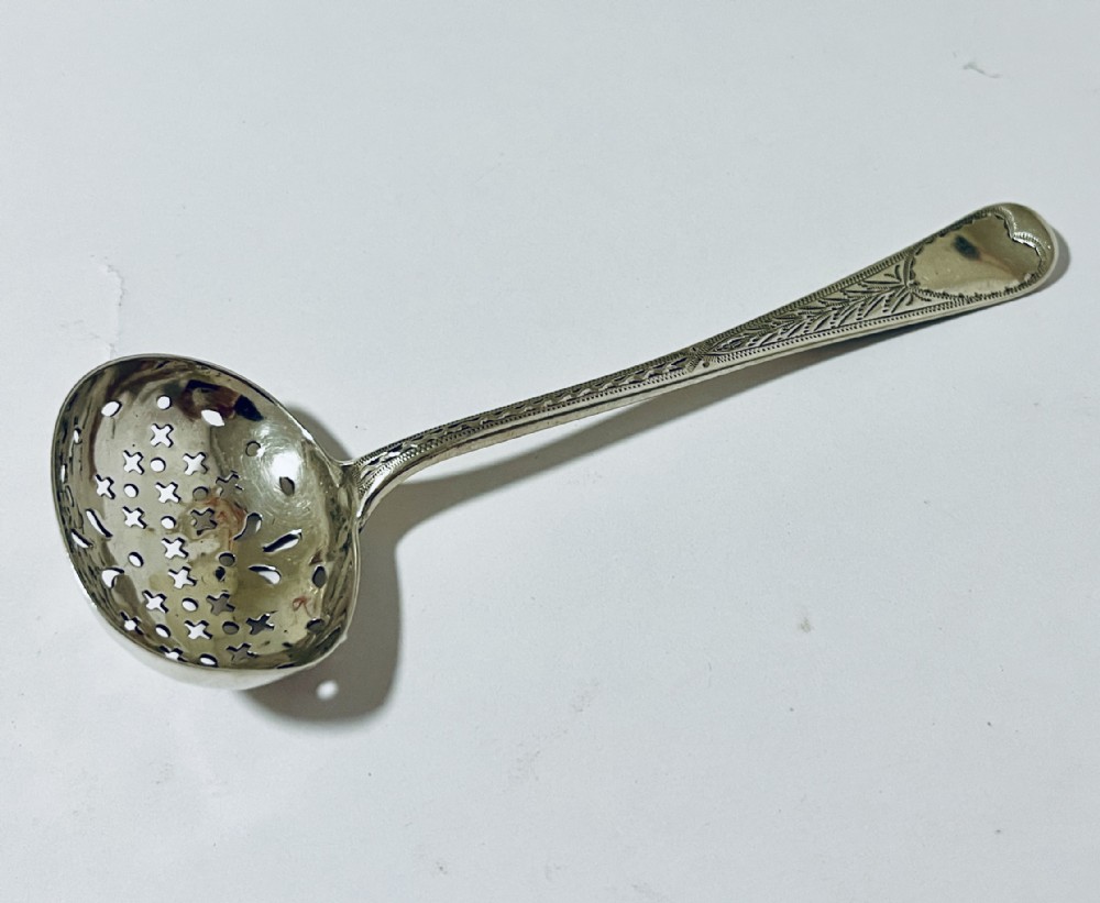 An antique Georgian silver sugar sifter spoon featuring a pierced bowl and an engraved handle.