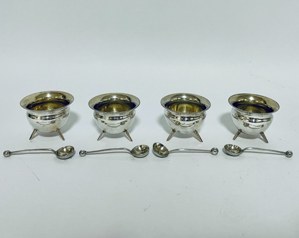 A set of four circular silver cauldron-shaped open salt cellars with beaded rims, tripod feet, and matching miniature ball-top spoons. View II