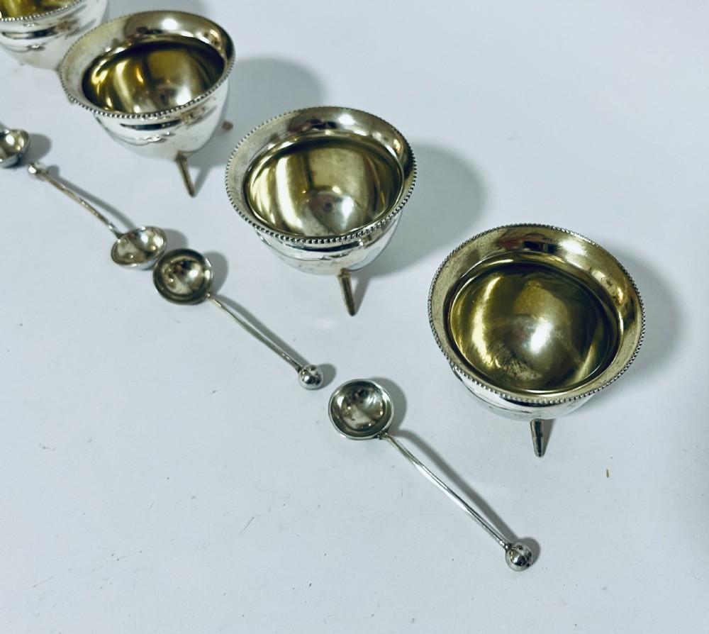 A set of four circular silver cauldron-shaped open salt cellars with beaded rims, tripod feet, and matching miniature ball-top spoons. View IV