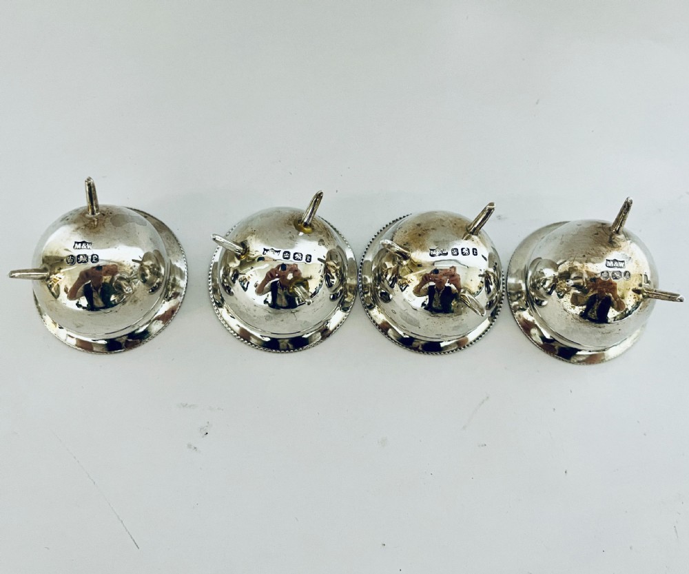A set of four circular silver cauldron-shaped open salt cellars with beaded rims, tripod feet, and matching miniature ball-top spoons. View VI