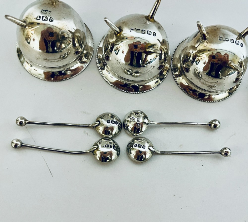 A set of four circular silver cauldron-shaped open salt cellars with beaded rims, tripod feet, and matching miniature ball-top spoons. View VII