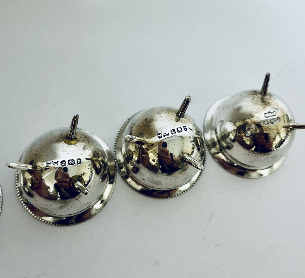 A set of four circular silver cauldron-shaped open salt cellars with beaded rims, tripod feet, and matching miniature ball-top spoons. View IX