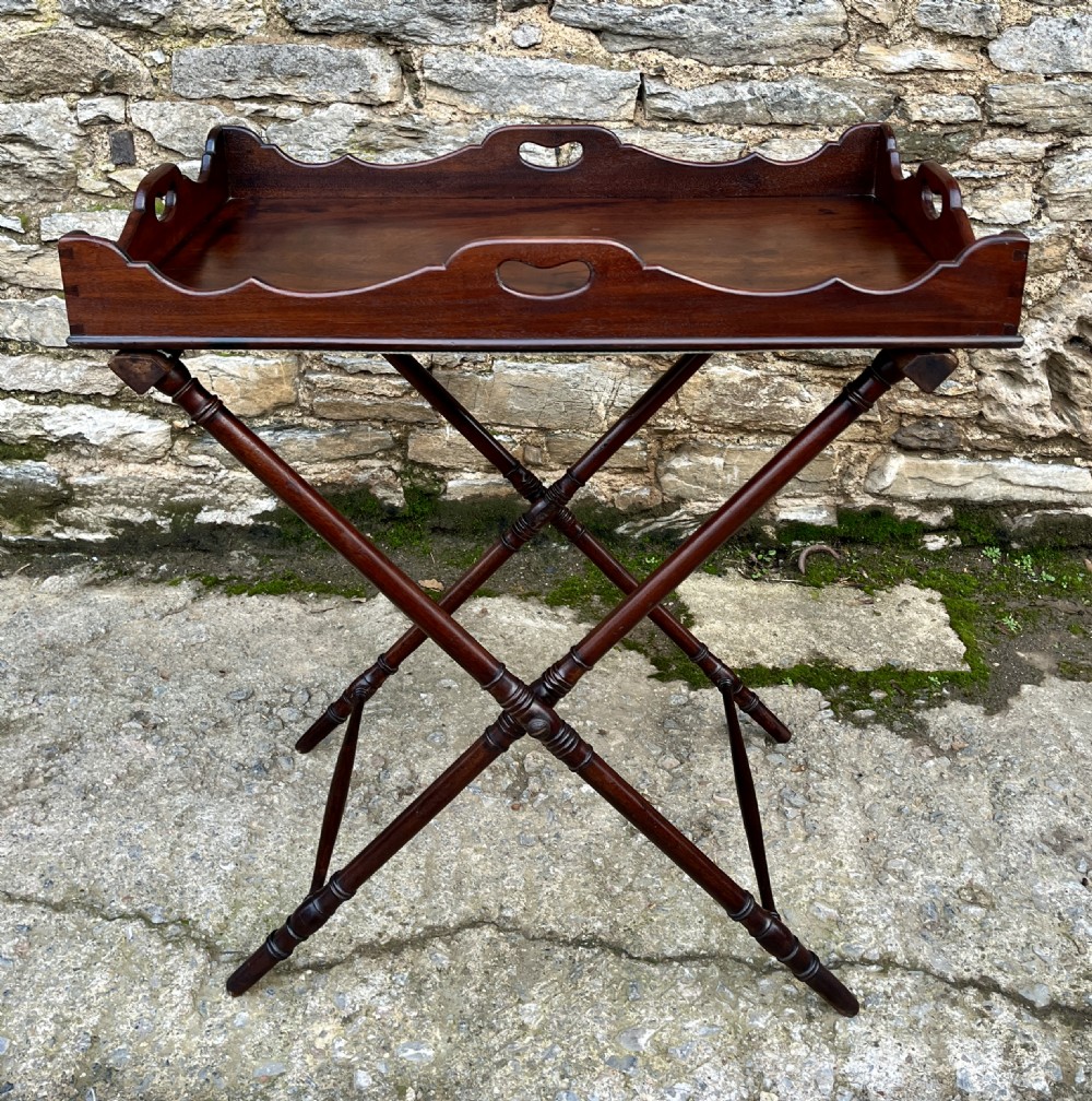 A Georgian mahogany folding butlers tray table with a scalloped gallery border, heart-shaped cut-out handles, and a turned X-frame stand.