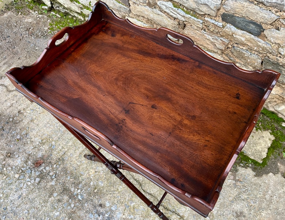 A Georgian mahogany folding butlers tray table with a scalloped gallery border, heart-shaped cut-out handles, and a turned X-frame stand. View IX