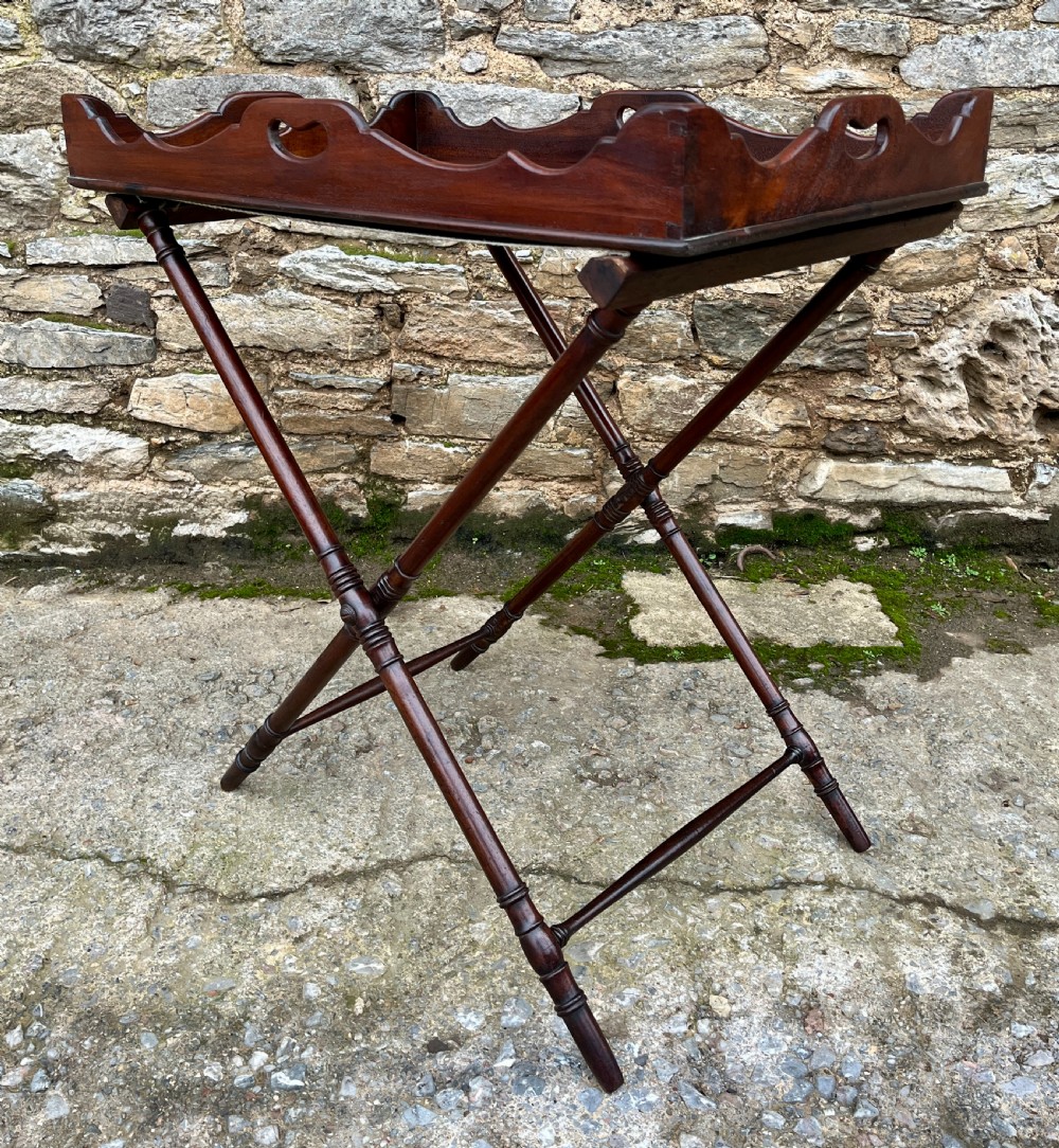 A Georgian mahogany folding butlers tray table with a scalloped gallery border, heart-shaped cut-out handles, and a turned X-frame stand. View X