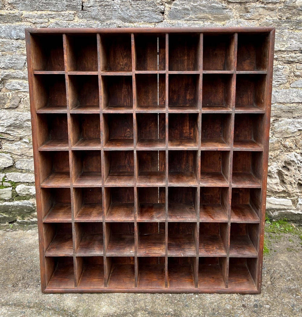 A large square wooden storage unit featuring a six-by-six grid of thirty-six rectangular cubbies made of dark stained pine.
