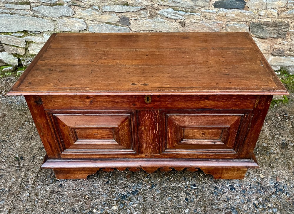 A solid oak blanket chest featuring dual fielded front panels, a central brass keyhole escutcheon, and a carved decorative apron along the base. View II