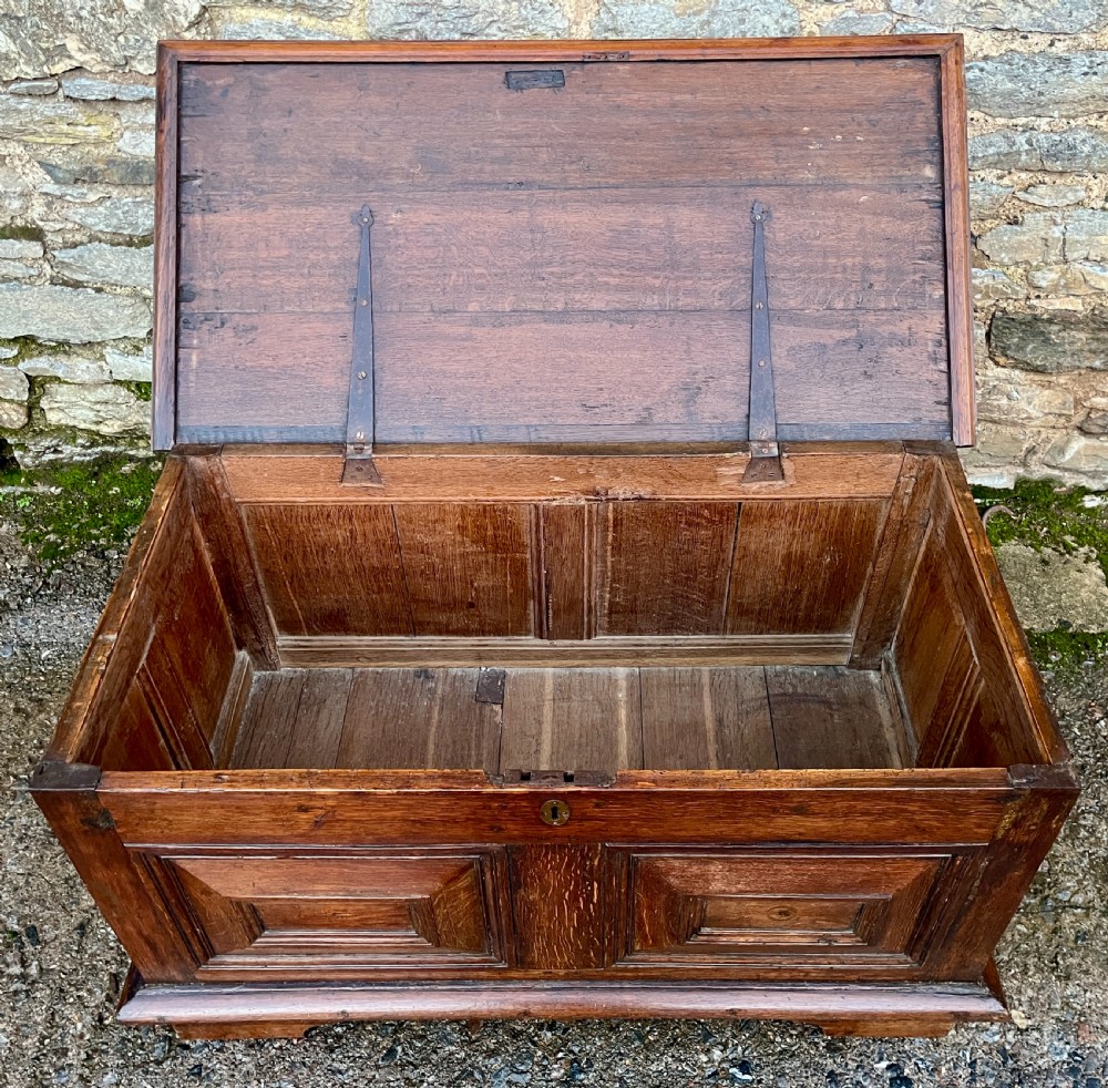 A solid oak blanket chest featuring dual fielded front panels, a central brass keyhole escutcheon, and a carved decorative apron along the base. View V