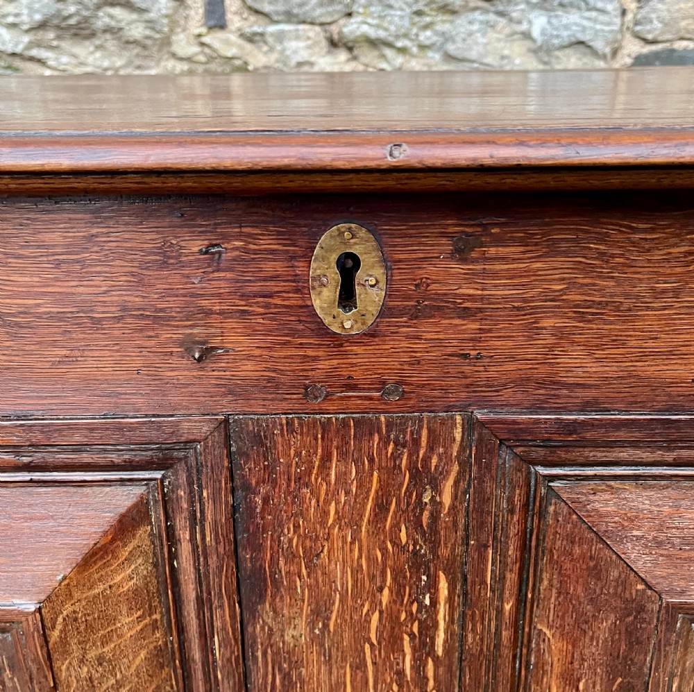A solid oak blanket chest featuring dual fielded front panels, a central brass keyhole escutcheon, and a carved decorative apron along the base. View X